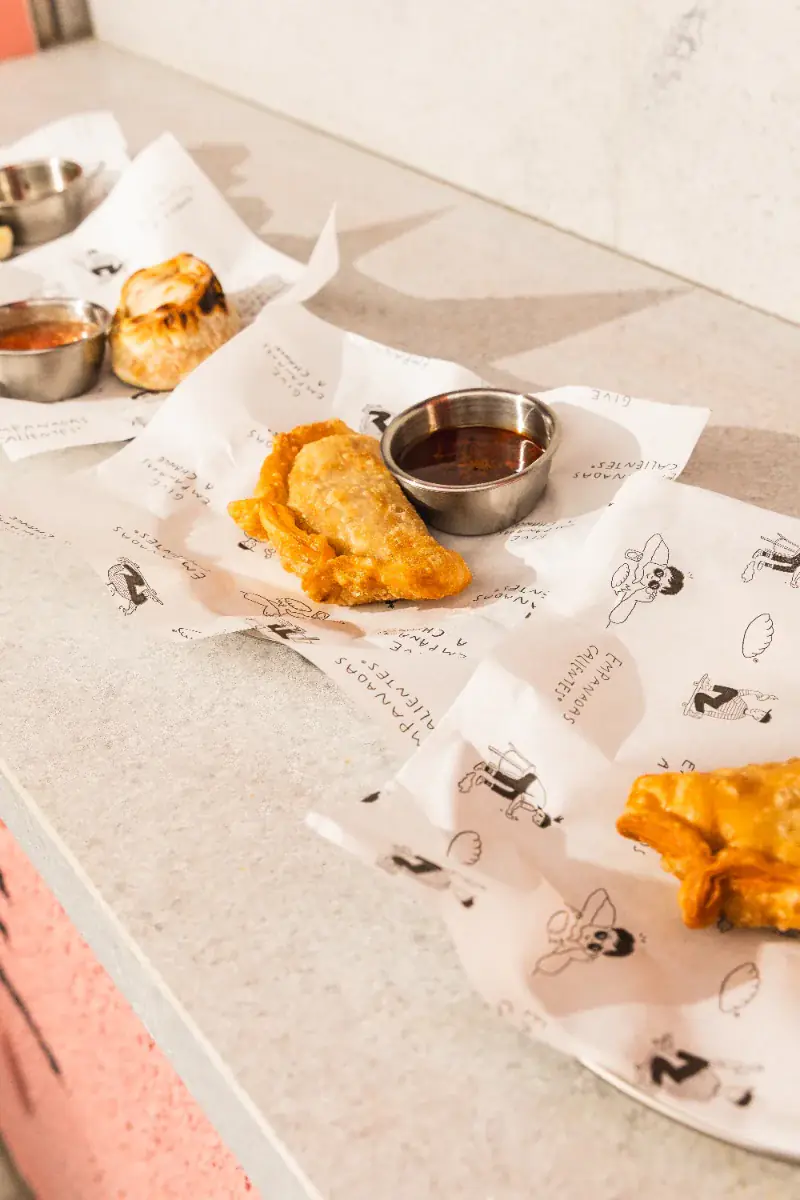 Empanadas sobre papel de la marca, con una salsa para mojar al costado