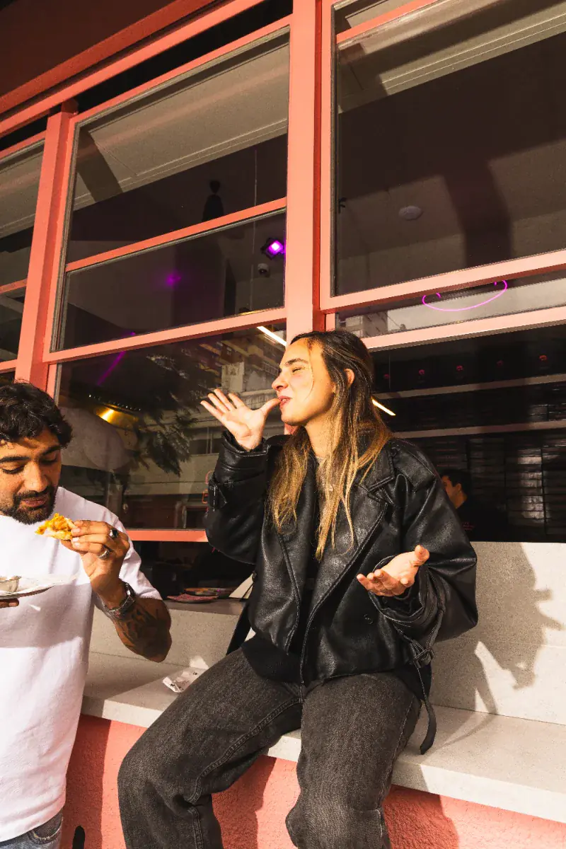 Dos personas comiendo empanadas sentadas frente al local de frente rosa, en Belgrano