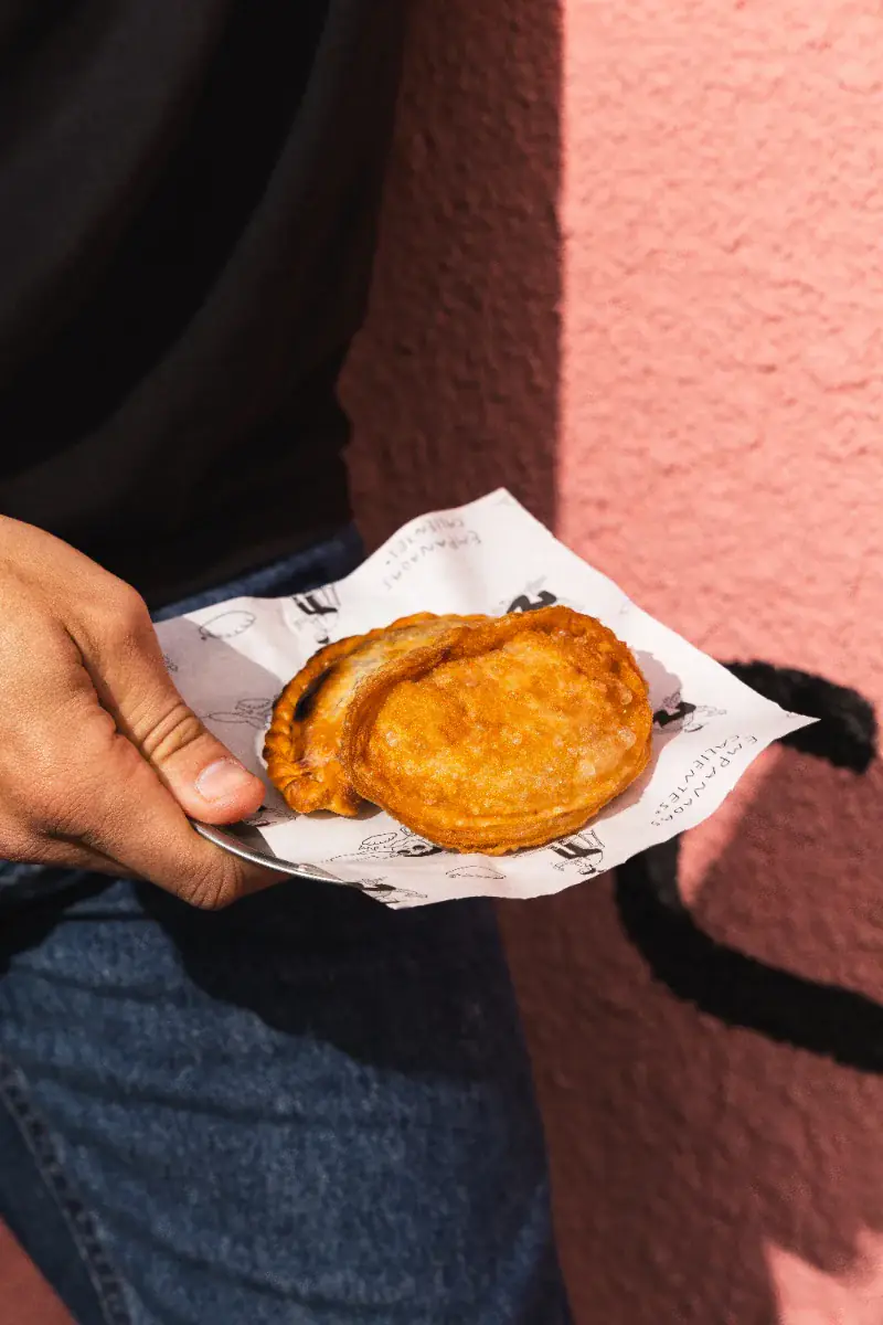 Empanadas apoyadas sobre papel de la marca contra la pared rosa del local